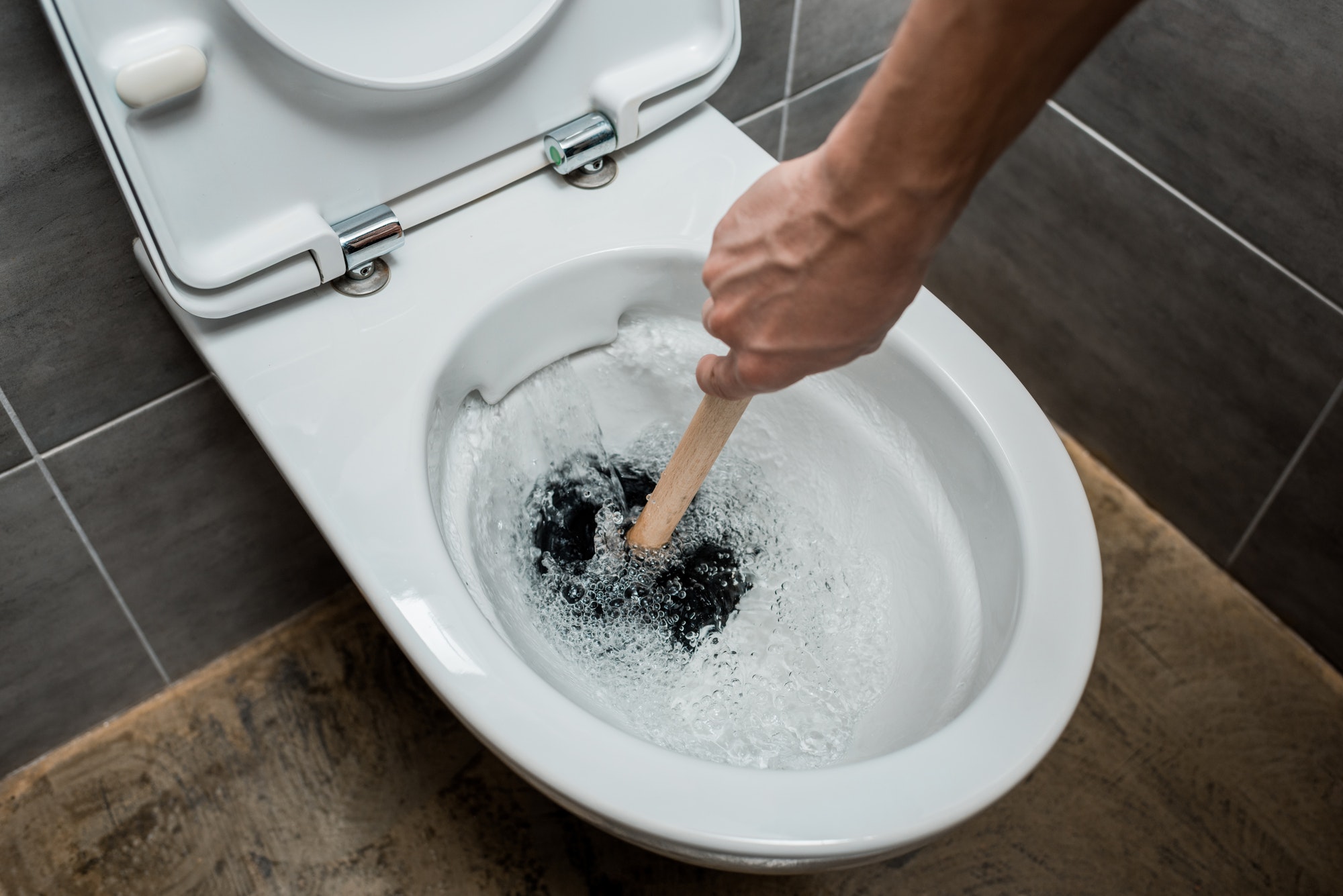 cropped view of plumber using plunger in toilet bowl during flushing in modern restroom with grey